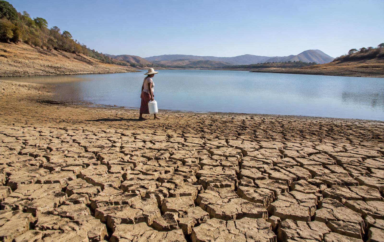 A person crosses exposed reservoir ground to collect water